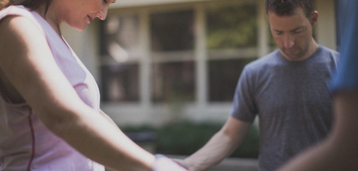 Stock photo of a group of at least three people holding hands in a circle and praying outside