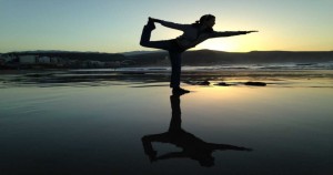 Silhouette of a woman striking a balanced yoga pose on a beach