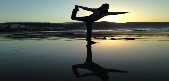 Silhouette of a woman striking a balanced yoga pose on a beach