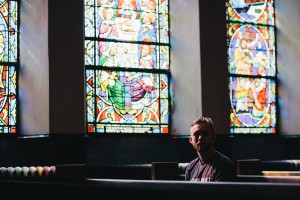 Man sitting alone in a pew in front of stained glass windows