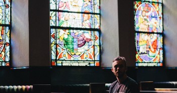 Man sitting alone in a pew in front of stained glass windows