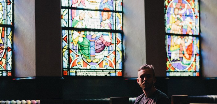 Man sitting alone in a pew in front of stained glass windows