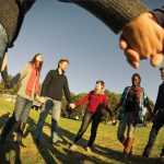 Photo of a diverse group of younger people smiling and holding hands in a sunny meadow