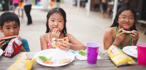 Photo of smiling kids eating at a picnic table