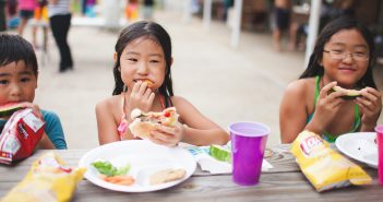 Photo of smiling kids eating at a picnic table