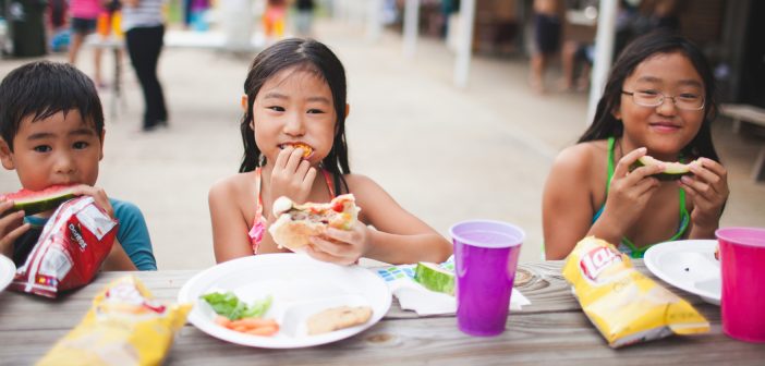 Photo of smiling kids eating at a picnic table