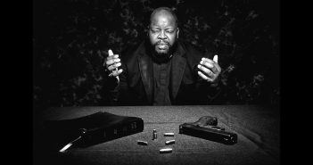 Photo of a man in prayer in front of a bible and a hand gun