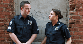 Two police officers having a conversation outside near the side of building
