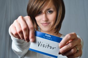 Woman holding up a nametag that reads Hello, my name is visitor