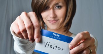 Woman holding up a nametag that reads Hello, my name is visitor