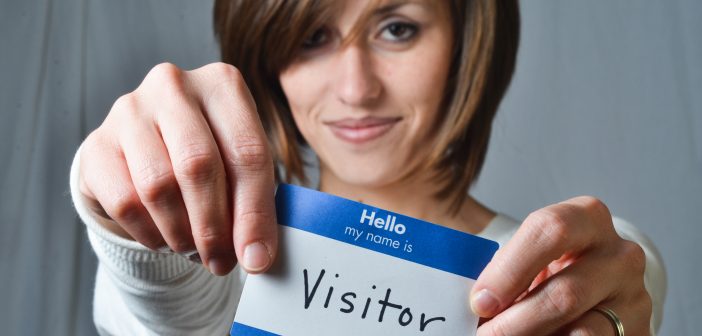 Woman holding up a nametag that reads Hello, my name is visitor