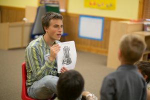 A young adult reading to a group of kids and engaged in his church's partnership with the local school