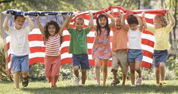 Photo of a diverse group of children running with an American flag, which highlights the coming demographic shift. CREDIT: Ariel Skelley / Blend / Learning Pictures / Universal Images Group