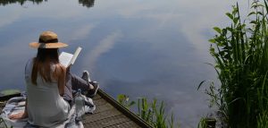 Photo of a person reading a book on a lakeside dock