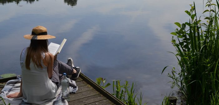 Photo of a person reading a book on a lakeside dock