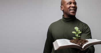 Photo of a person holding an open Bible with a seedling sprouting from the pages