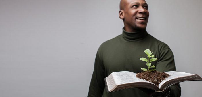 Photo of a person holding an open Bible with a seedling sprouting from the pages