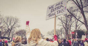 Photo of person at a protest rally with a sign that reads "We are better than this!"
