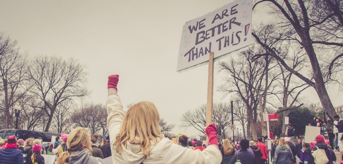 Photo of person at a protest rally with a sign that reads "We are better than this!"