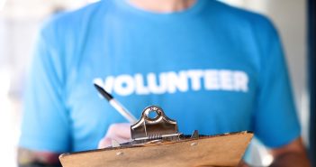 Photo of a person wearing a "Volunteer" t-shirt writing on a clipboard