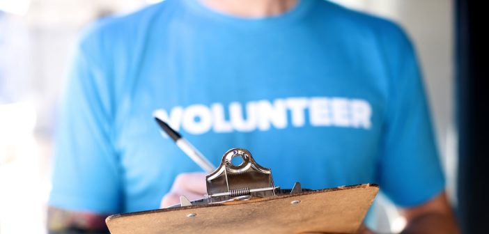 Photo of a person wearing a "Volunteer" t-shirt writing on a clipboard