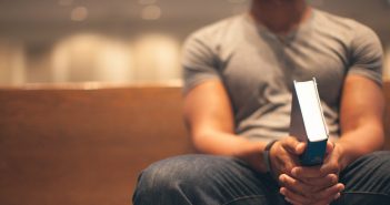 Photo of a face-unseen millennial sitting in a pew holding a Bible