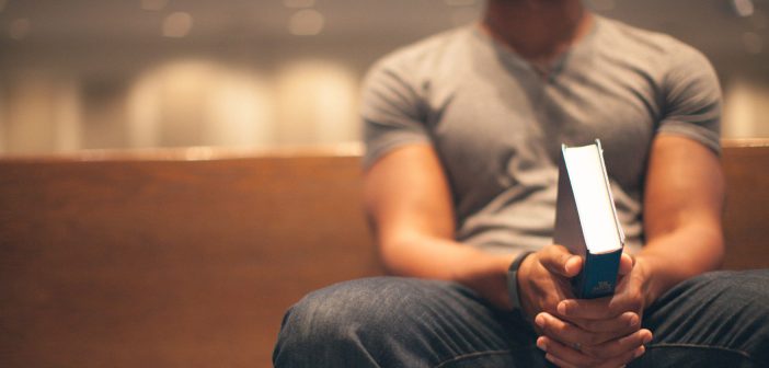 Photo of a face-unseen millennial sitting in a pew holding a Bible