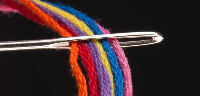 Photo of threads of many colors passing through the eye of a needle