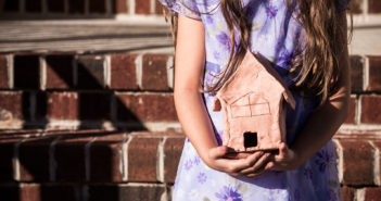 Child holding a clay model of a building while standing on stairs in front of large building