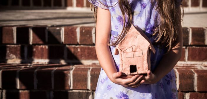 Child holding a clay model of a building while standing on stairs in front of large building