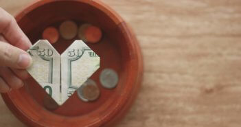 Hand holding a $50 bill folded into a heart over an offering plate