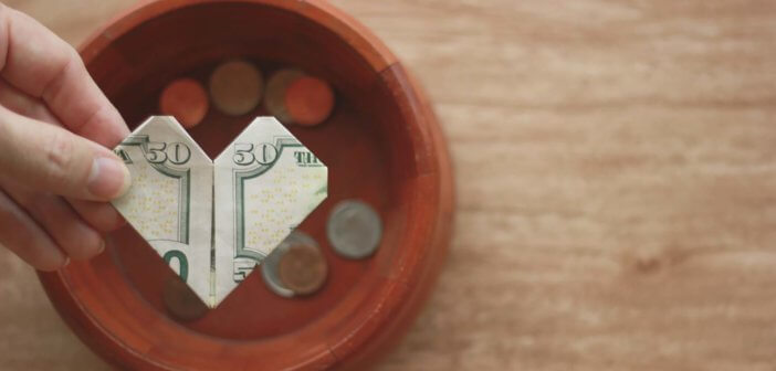 Hand holding a $50 bill folded into a heart over an offering plate