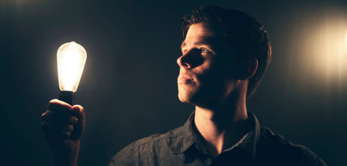 Person holding a brightly lit light bulb in a dark room