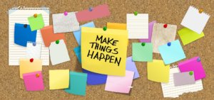 Photo of sticky notes on a bulletin board, one reading "Make Things Happen"