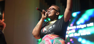 Person with a tattoo visible on their arm and wearing a t-shirt singing joyfully at church