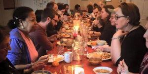 People sitting at a long table having animated conversations while eating dinner at Simple Church in Massachusetts
