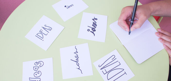 Person writing in a notebook on a table covered with index cards that say IDEAS