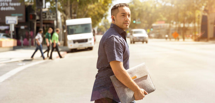 Young pastor carrying a laptop bag while crossing a city street
