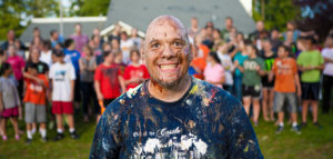 Grinning paint-spattered church youth leader standing in front of a group of youth