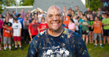 Grinning paint-spattered church youth leader standing in front of a group of youth