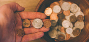 Close up of a hand dropping coins into a collection plate