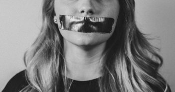 Black and white photo of a woman silenced by tape covering her mouth