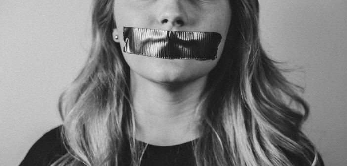 Black and white photo of a woman silenced by tape covering her mouth