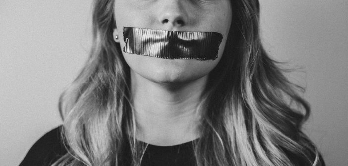 Black and white photo of a woman silenced by tape covering her mouth