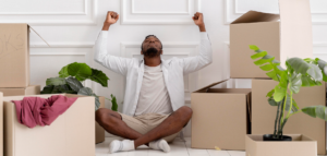 Pastor sitting among moving boxes with their arms raised in happiness