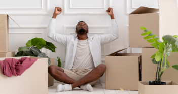 Pastor sitting among moving boxes with their arms raised in happiness