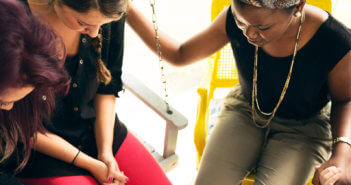 People holding hands in prayer while sitting on a front porch