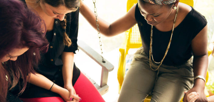 People holding hands in prayer while sitting on a front porch