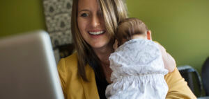 Parent typing on a computer while holding their infant
