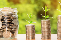 Jar of coins beside growing stacks of coins with seedlings sprouting from the top